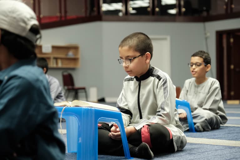 Student reading the Quran from a low desk at Abu Huraira Center