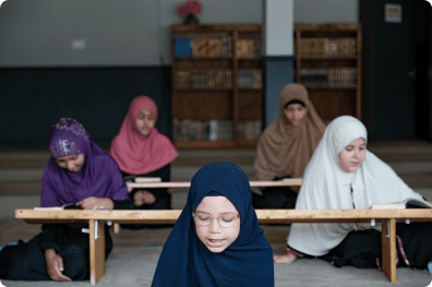 Girls reading the Quran at long wooden desks